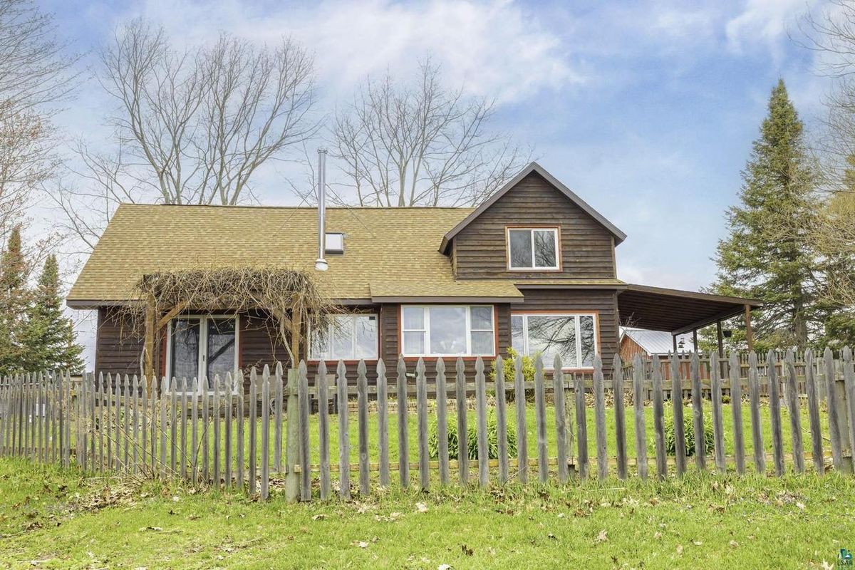 The farmhouse from the yard, with dark wood siding, a covered porch, and a weathered picket fence.