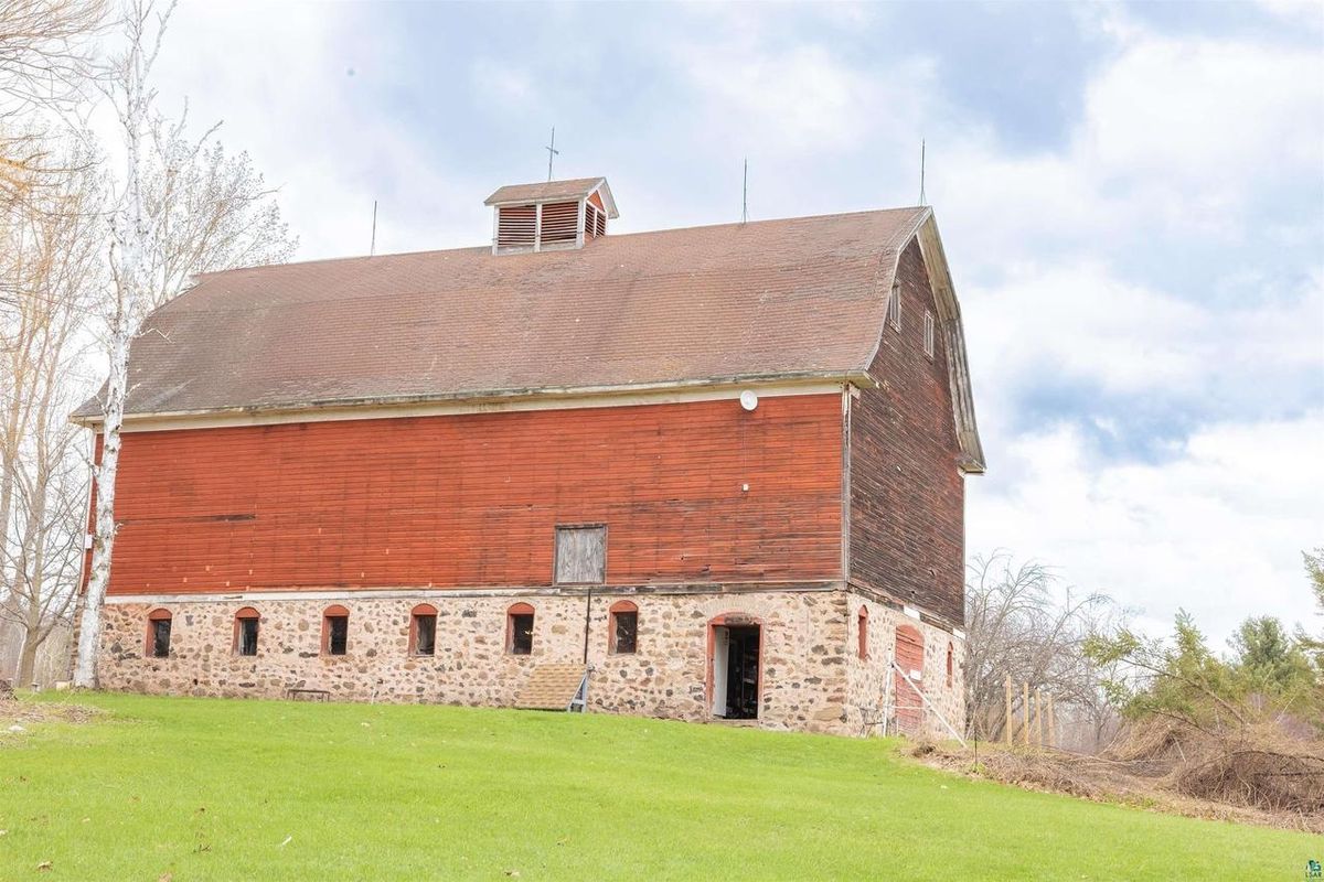 The barn from the field side, with its red siding, stone foundation, and cupola.